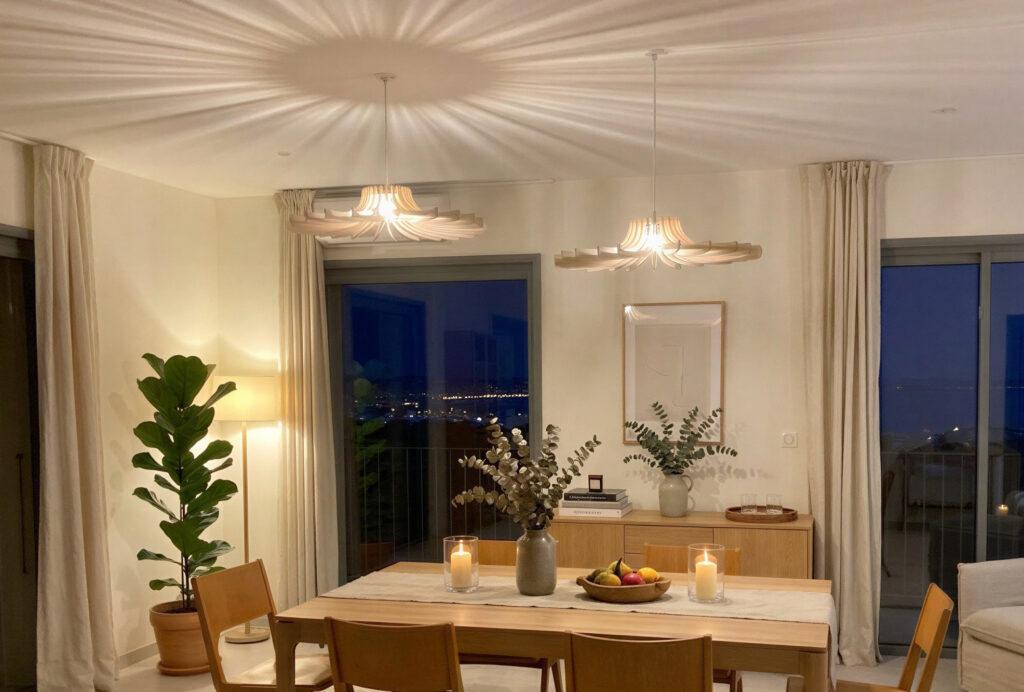 Deux luminaires suspendus en bois dans un salon le soir, au dessus de la table à manger