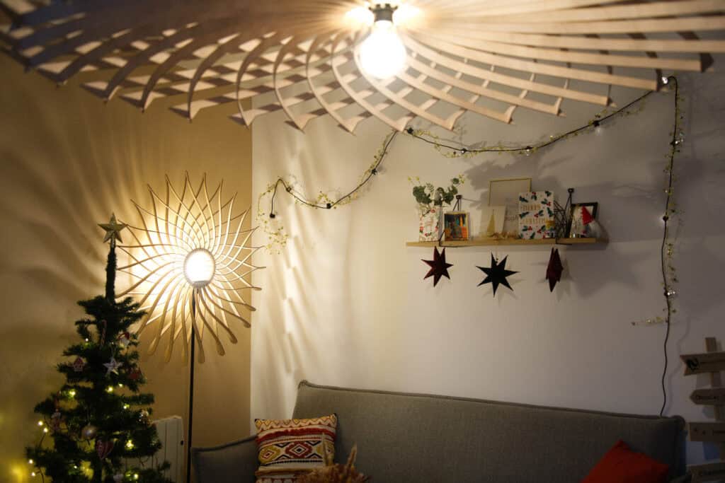 Suspension en bois découpé au laser et lampadaire soleil Atelier Sapi dans un salon décoré pour Noël, avec sapin et guirlandes