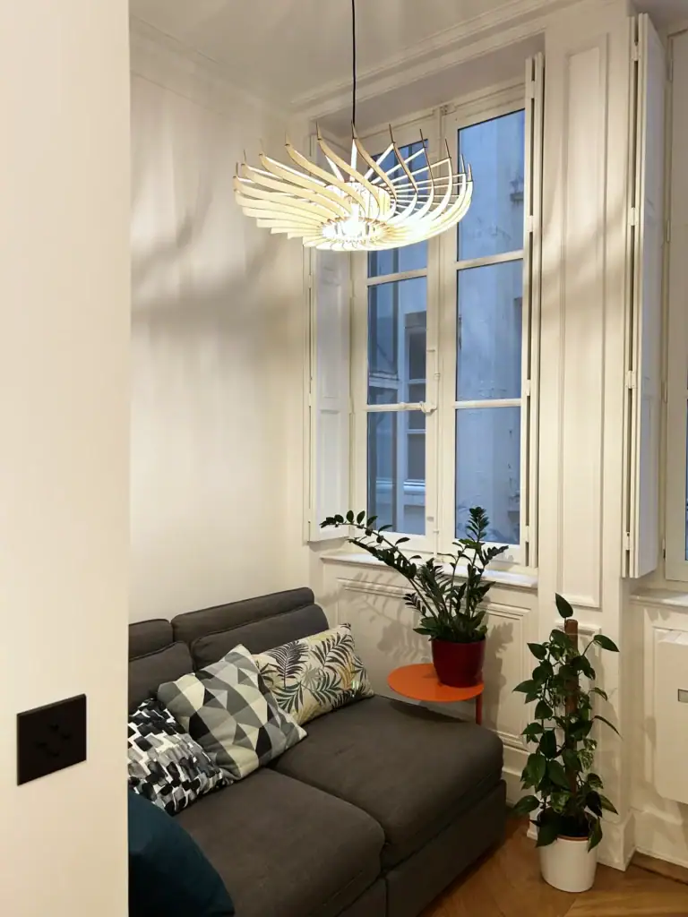 Suspension en bois Claudine la turbine au-dessus d'un canapé devant une grande fenêtre haussmannienne