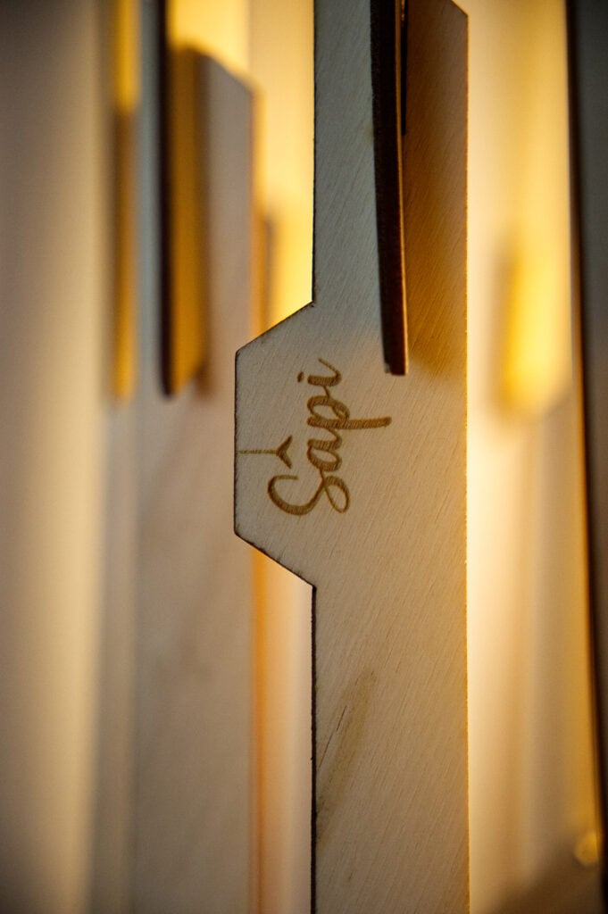 Gros plan extrême sur la gravure laser du logo Sâpi sur une lame de bois poncée à la main.