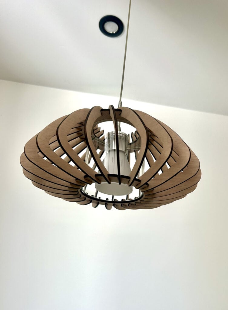Suspension en bois éclairée vue de dessous avec sa structure en lamelles courbes – Atelier Sâpi