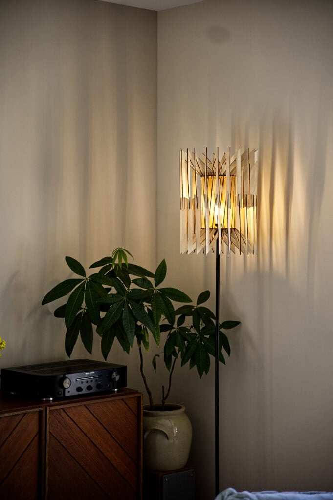 Lampadaire en bois Léon dans un salon, avec une grande plante verte et un meuble enfilade vintage.