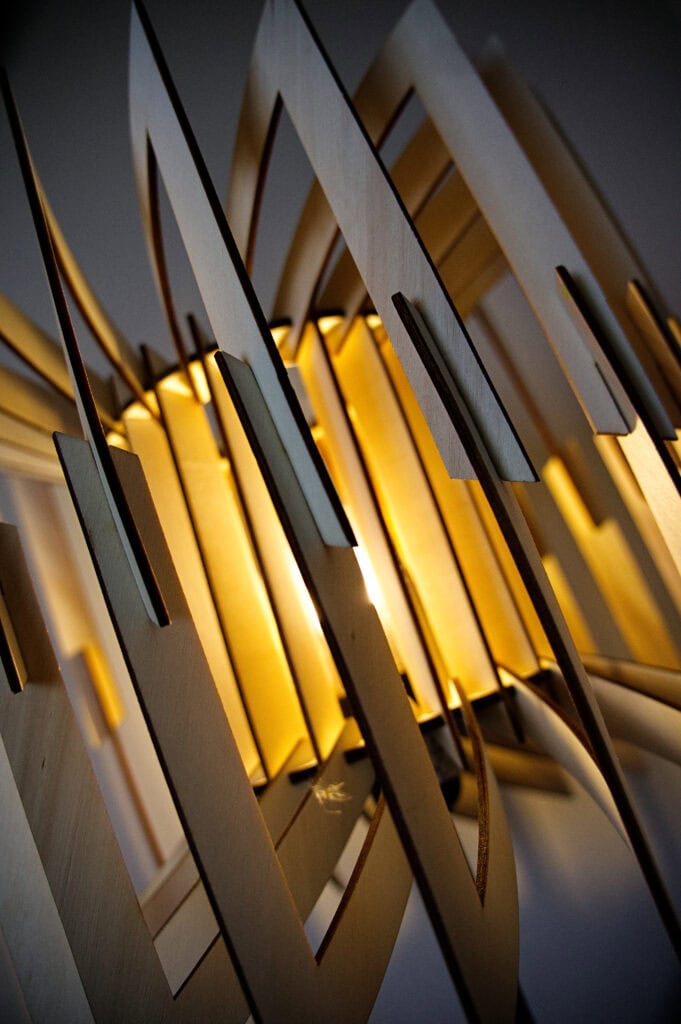 Gros plan des emboîtements en bois à l'intérieur du lampadaire Léon, baignés par la lumière chaude de l'ampoule.